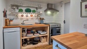 A compact kitchen with a dishwasher, stove, and wooden countertop. - The Noel at Lesceave (Praa Sands)