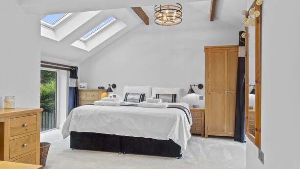 A bedroom with a skylight, a bed with white bedding, a wooden wardrobe, and a bedside table with a lamp.