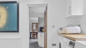 A modern kitchen with a built-in washing machine, a dining area with a wooden table and chairs, and a large framed picture on the wall.