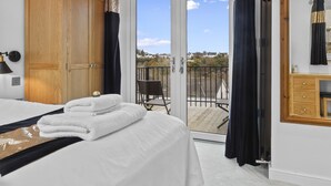 A bedroom with a bed, a wooden wardrobe, a balcony with a chair, and a large mirror.