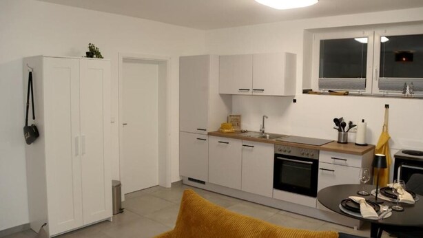 Una cocina compacta con gabinetes blancos, una estufa y un comedor con una mesa lista para dos.
