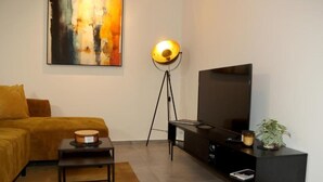 Una sala de estar moderna con sofá, una mesita, una lámpara de pie, televisor y una planta.