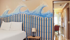 A hotel room with a bed, a nightstand with a lamp, and a wall with a blue wave painting. - ☀️2BR-Pet Friendly-1 Block from Beach-Off The Hook☀️ (St. Joe Beach)