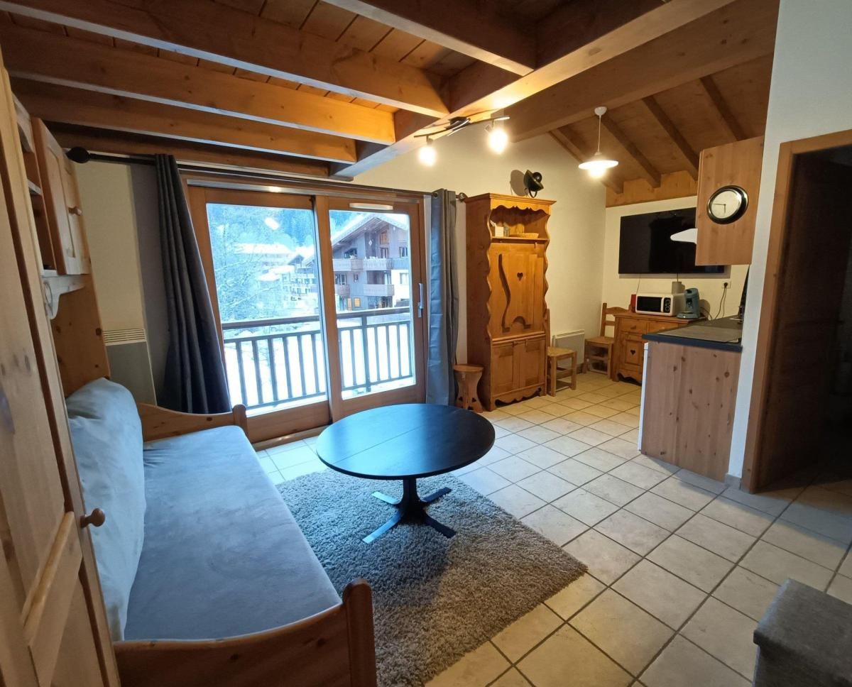 Une pièce confortable comprenant un lit, une table ronde, un coin cuisine et un balcon avec vue sur les immeubles.