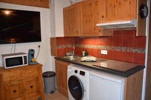 A compact kitchen with wooden cabinets, a microwave, a coffee maker, a sink, and a washing machine.