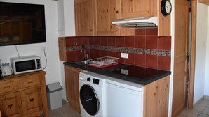 A compact kitchen with wooden cabinets, a microwave, a washing machine, and a tiled backsplash. - 200m from resort center, 1st floor, balcony, tv, ski locker, 26m², Pralognan-la-Vanoise (Pralognan-la-Vanoise)