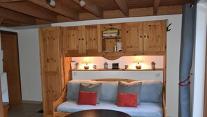 A cozy room with a wooden bench sofa, a round table, and a shelf with books and decorative items. - 200m from resort center, 1st floor, balcony, tv, ski locker, 26m², Pralognan-la-Vanoise (Pralognan-la-Vanoise)