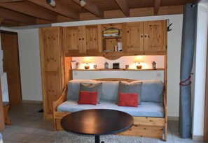 A cozy room with a wooden bench sofa, a round table, and a shelf with books and decorative items. - 200m from ski slopes, 1st floor, balcony, tv, ski locker, 26m², Pralognan-la-Vanoise (Pralognan-la-Vanoise)