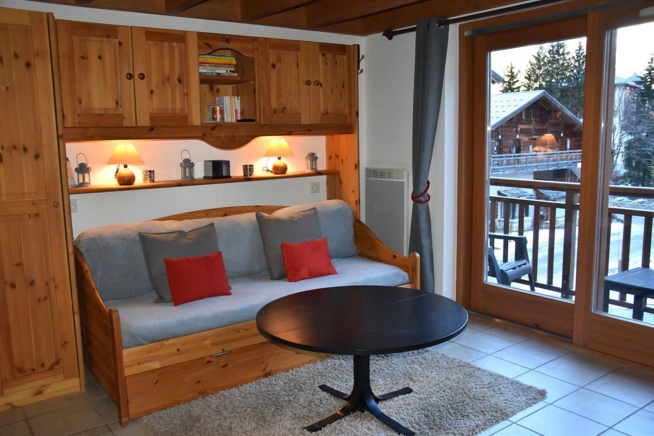 Ein gemütliches Zimmer mit einer Holzsofa, einem kleinen runden Tisch und Blick auf eine Holzhütte durch eine Glastür.