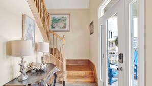 A wooden staircase leading to a balcony with blue chairs, a dining area with a table and chairs, and a framed picture on the wall. - Lagoon Front | Pet Friendly | Boat Launch, Pier and Beach Access (Gulf Shores)