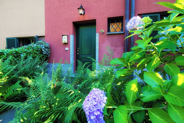 A building with a green door, a window with a lattice design, and a small potted plant on the wall. - Montorfano by the Lake (Montorfano)