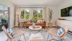 A living room with a sofa, two armchairs, a coffee table, and a view of a garden through large windows. - Gorgeous Home with Heated Pool Near Beaches (Seminole)