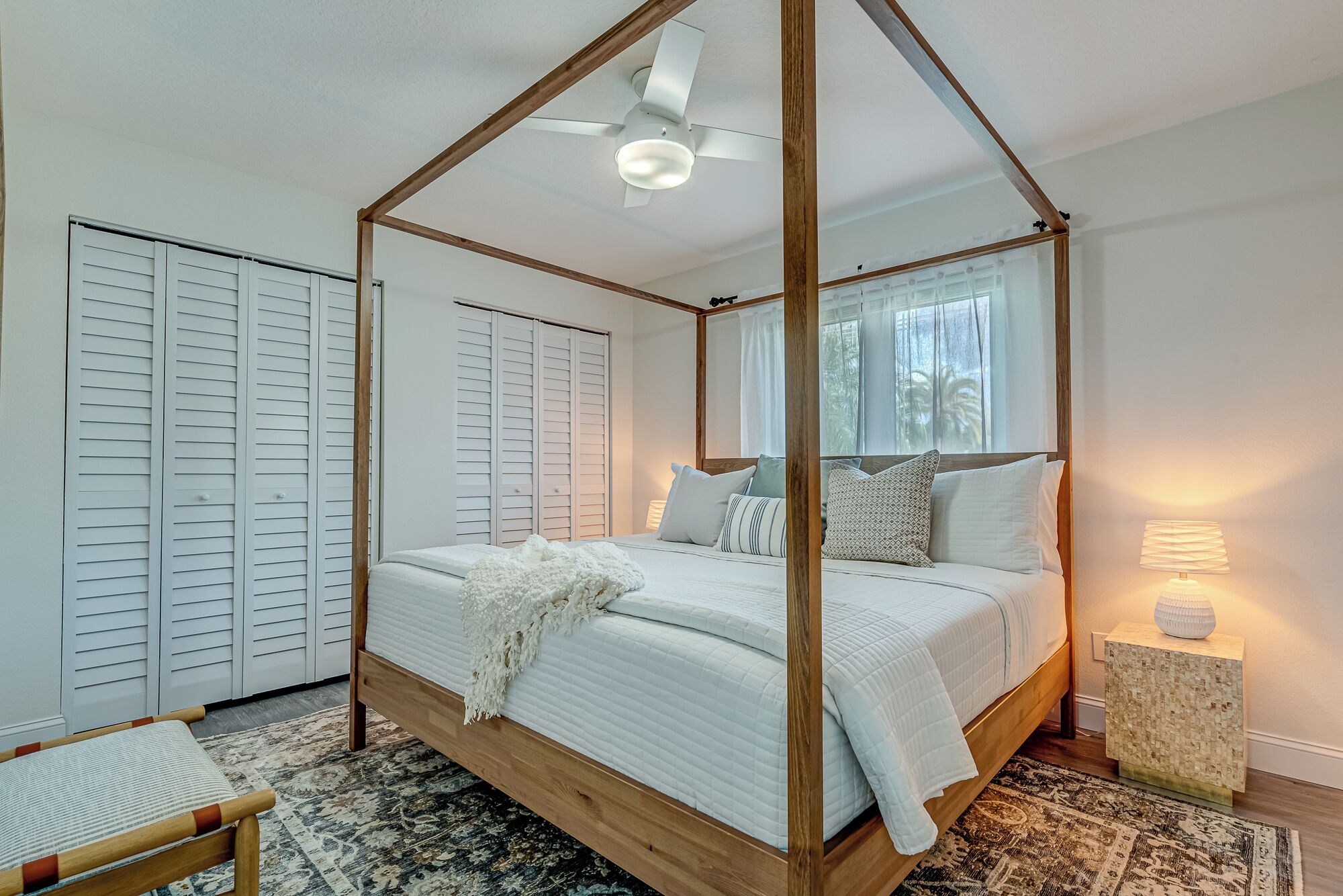 A four-poster canopy bed with a wooden frame, a ceiling fan, and a bedside lamp.