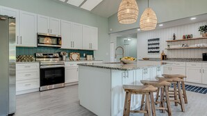 A modern kitchen with white cabinets, stainless steel appliances, a central island with stools, and pendant lighting. - Gorgeous Home with Heated Pool Near Beaches (Seminole)