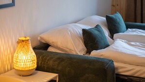 Een netjes opgemaakt slaapkamer met een bed, kussens en een nachtkastje met een lamp.