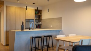 Een moderne keuken met een centraal kookeiland, barstoelen, een eettafel en hanglampen.