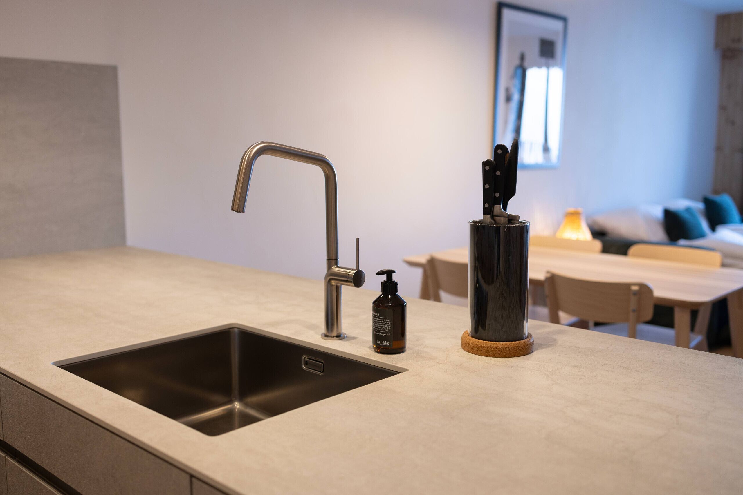 A modern kitchen with a stainless steel sink, a bottle of hand soap, and a knife block on the countertop.