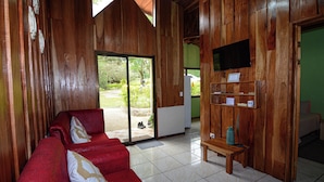 A wooden interior with a red sofa, a television mounted on the wall, and a sliding glass door leading to an outdoor area.