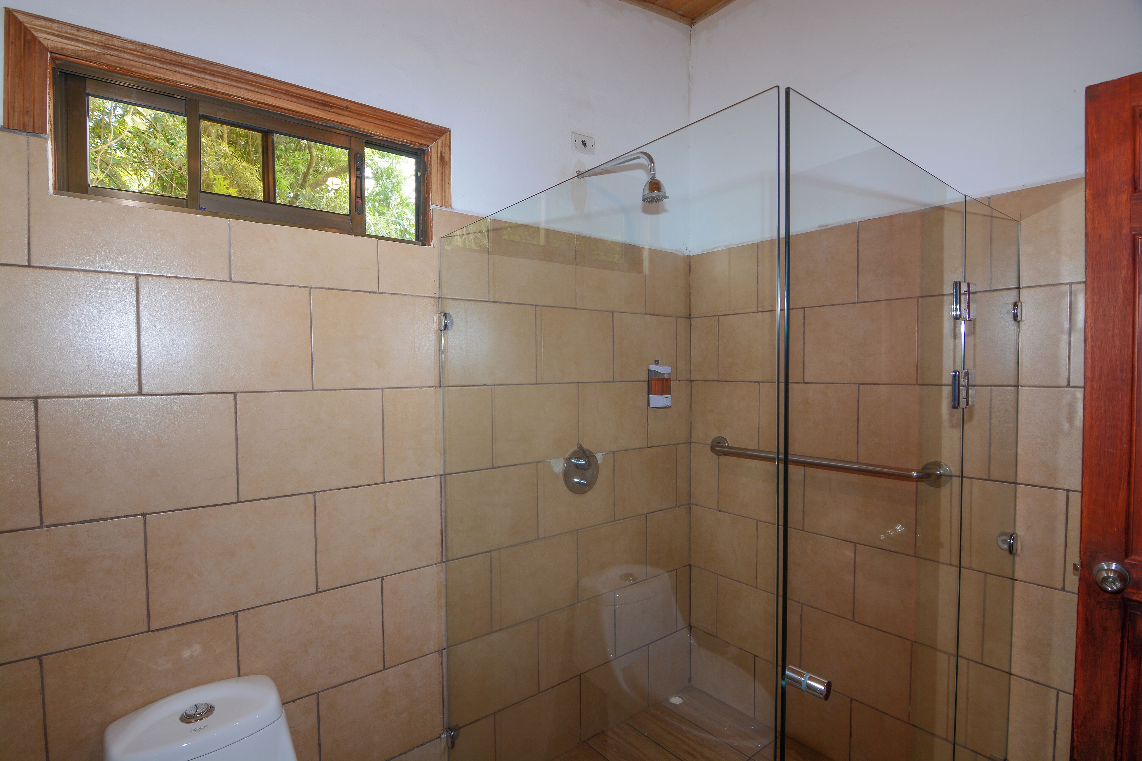 A bathroom with a glass shower enclosure, a toilet, and a window above the sink.