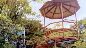 A gazebo with a roof and multiple levels, surrounded by grass and trees.