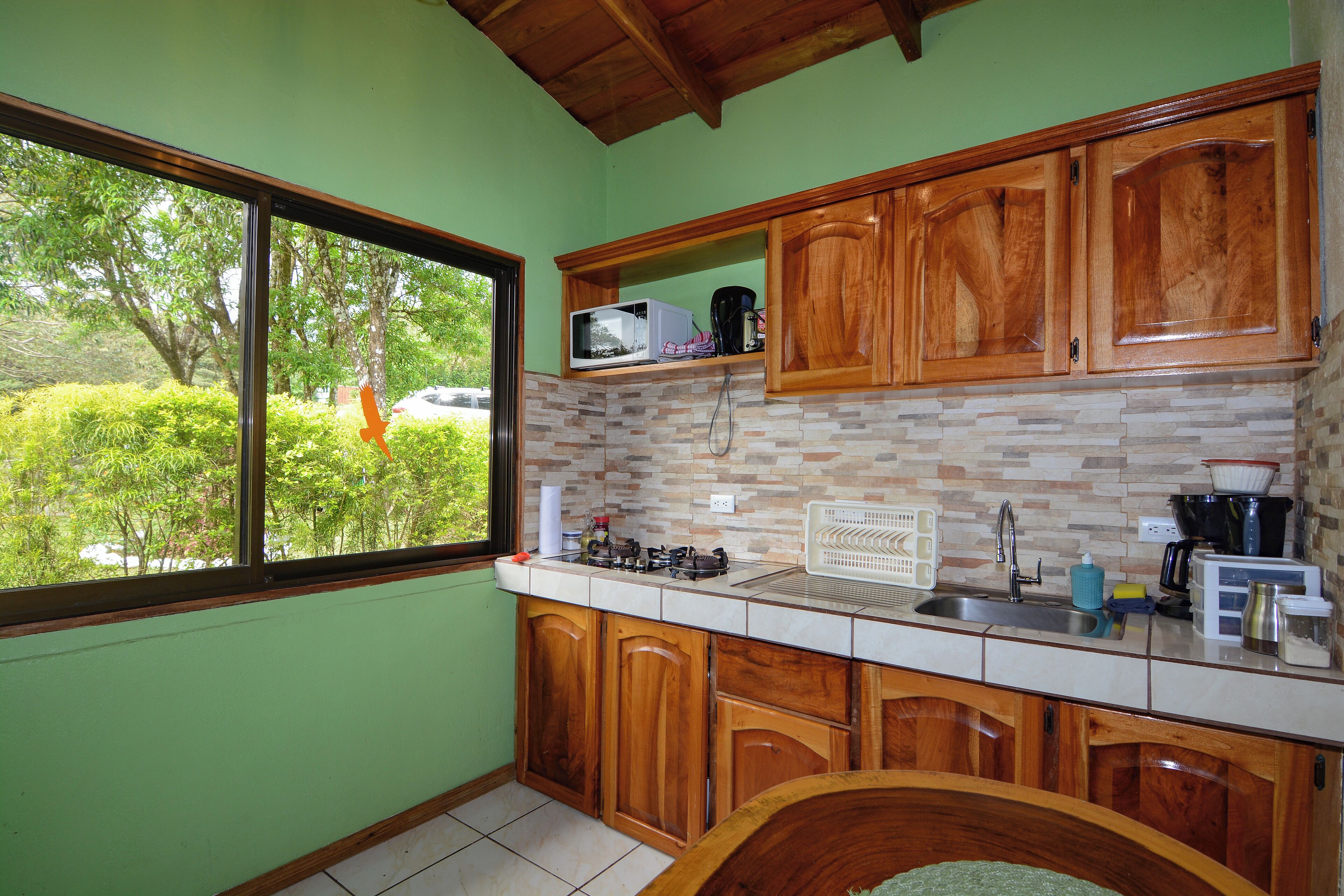 A kitchen with wooden cabinets, a microwave, and a window overlooking greenery.