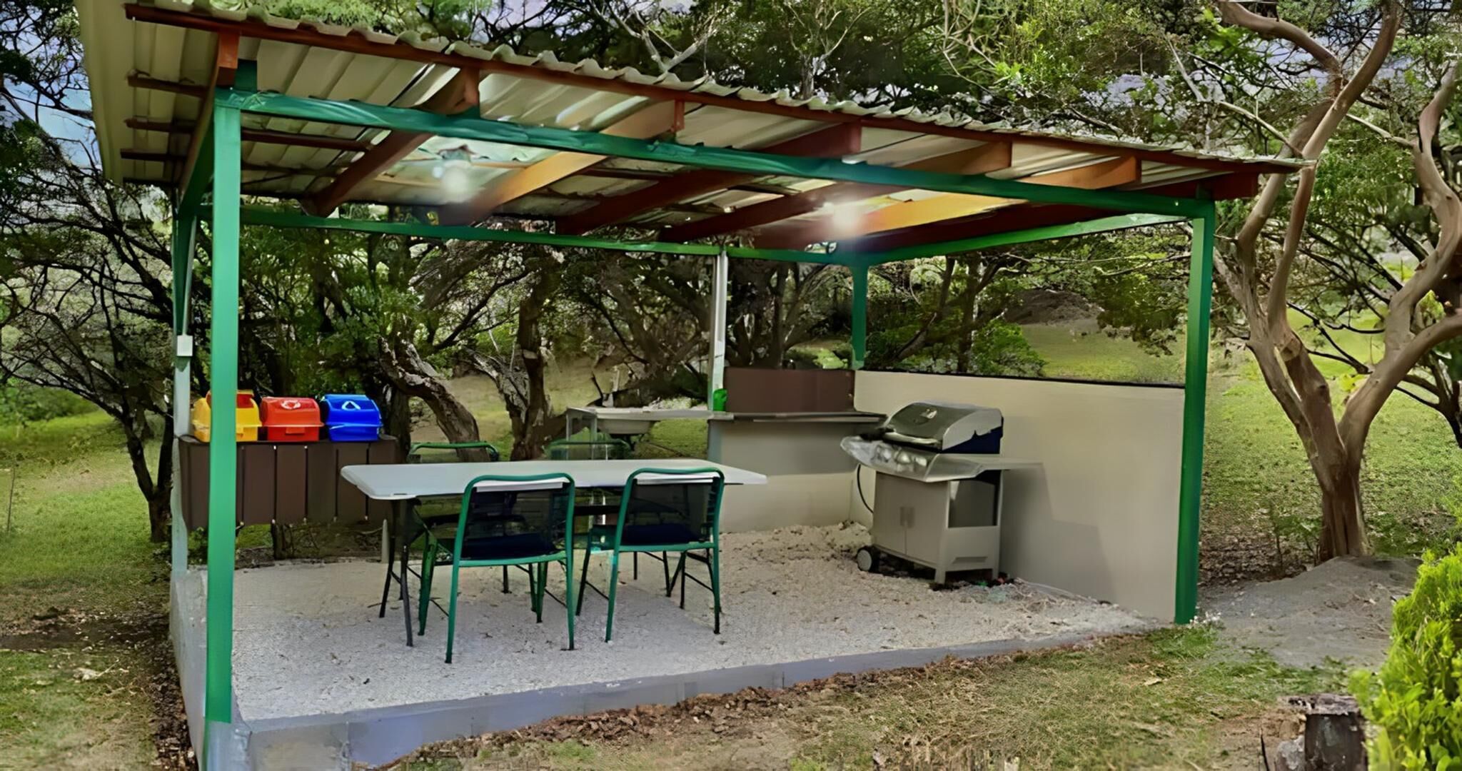 Ein überdachter Außenbereich mit Tisch, Stühlen, einem Grill und einer Mülltonne.