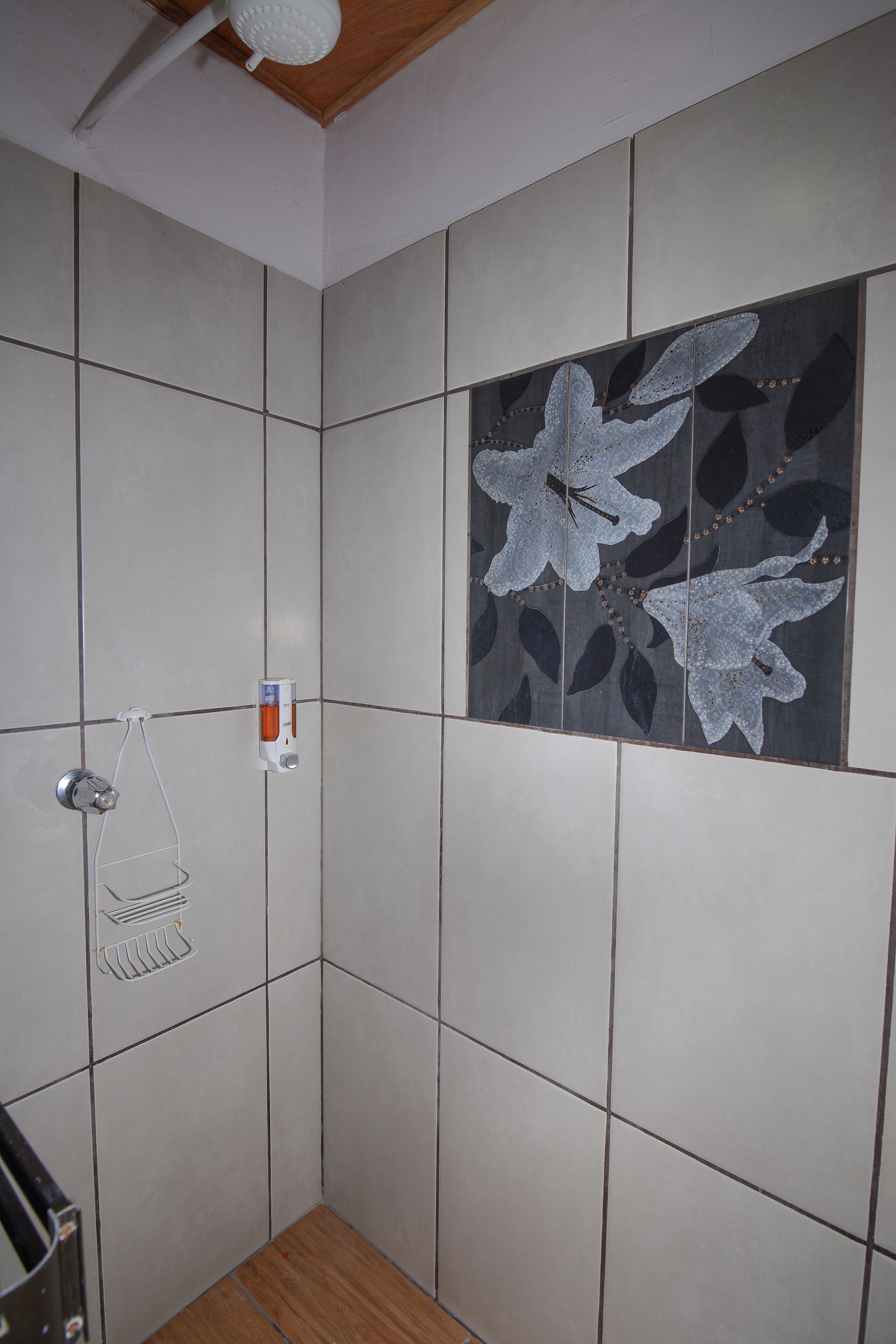 A shower with tiled walls and a wooden floor.