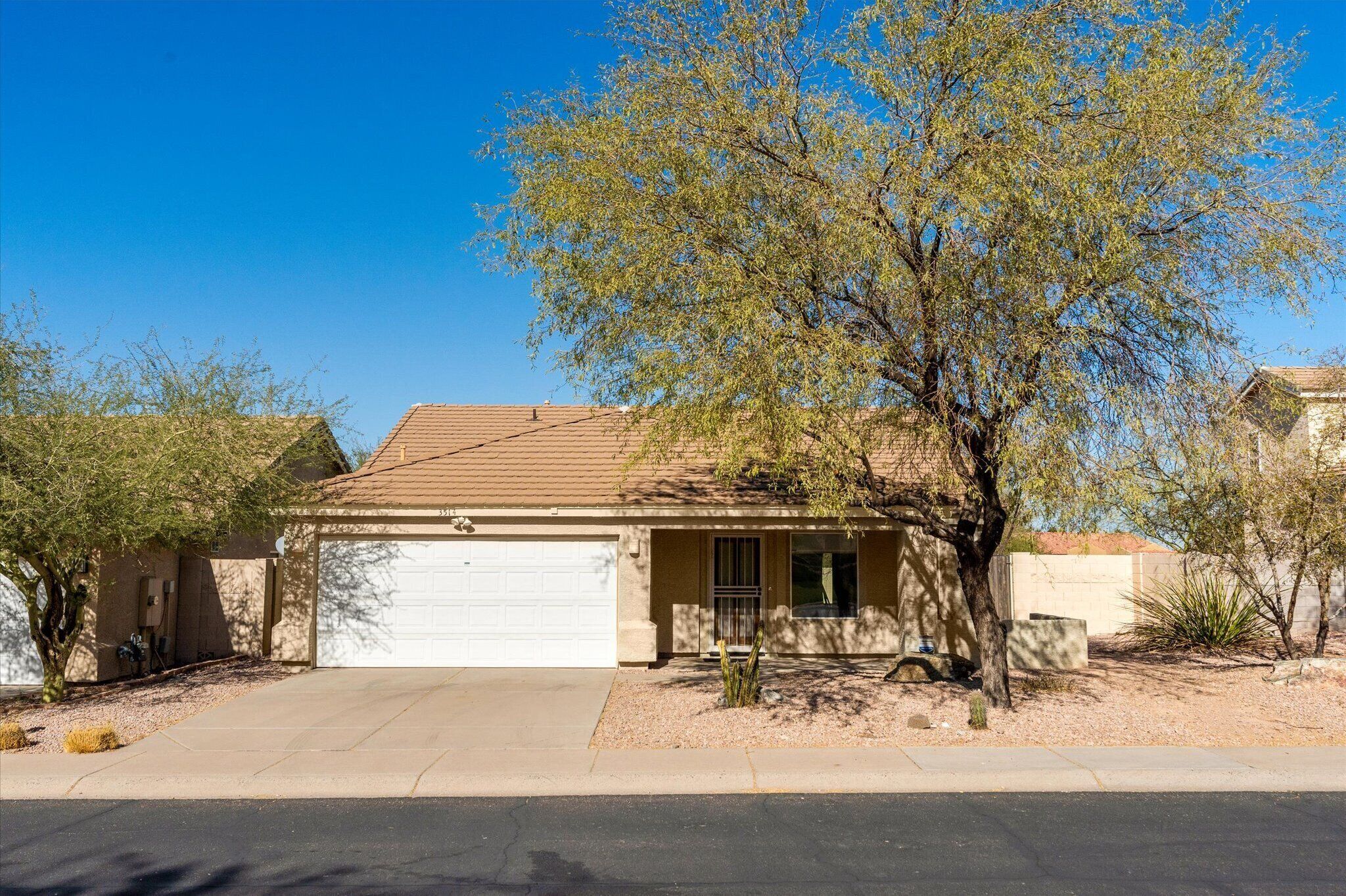 A single-story house with a garage, surrounded by desert vegetation and a clear blue sky.