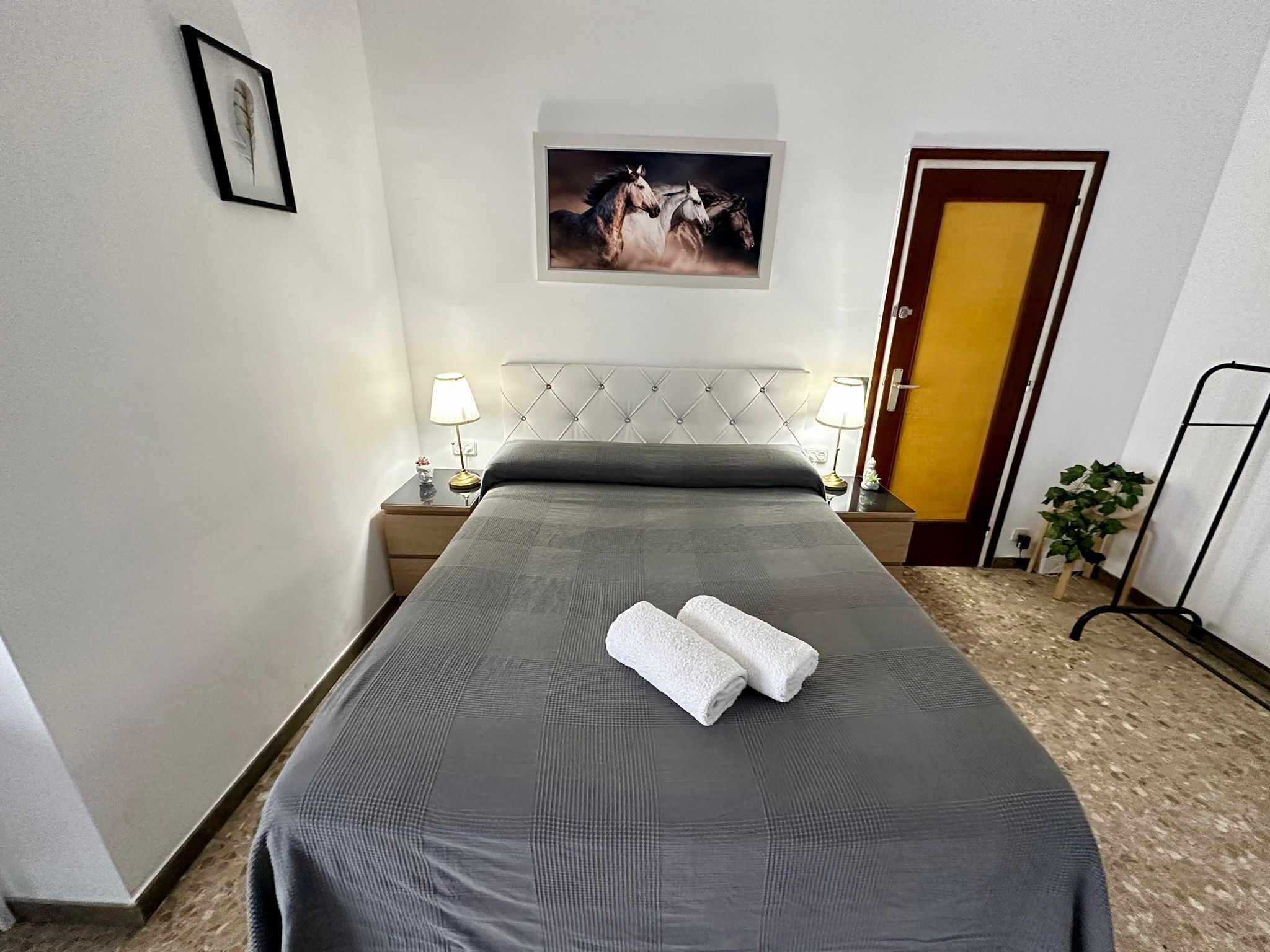 A hotel room with a bed, a nightstand with a lamp, a framed picture on the wall, and a door.