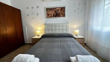 Habitación de hotel con una cama grande, dos mesitas de noche con lámparas, un armario de madera, un aire acondicionado de pared y un cuadro enmarcado de leones.
