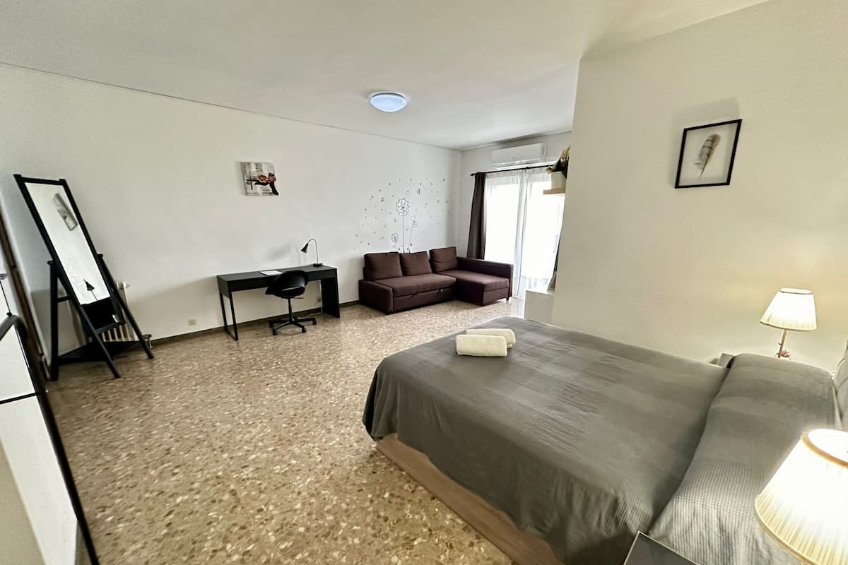 Una camera d'albergo con un letto, una scrivania, una sedia, un divano e una lampada da terra.