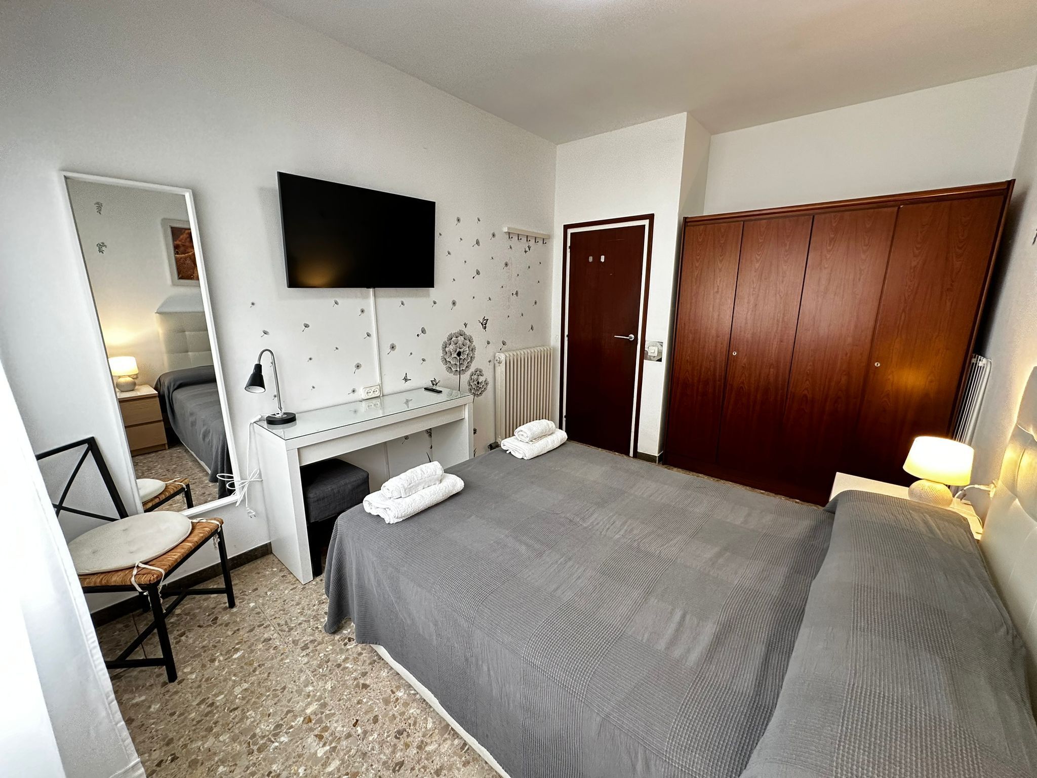 A hotel room with a bed, a desk, a chair, a TV, and a wardrobe.
