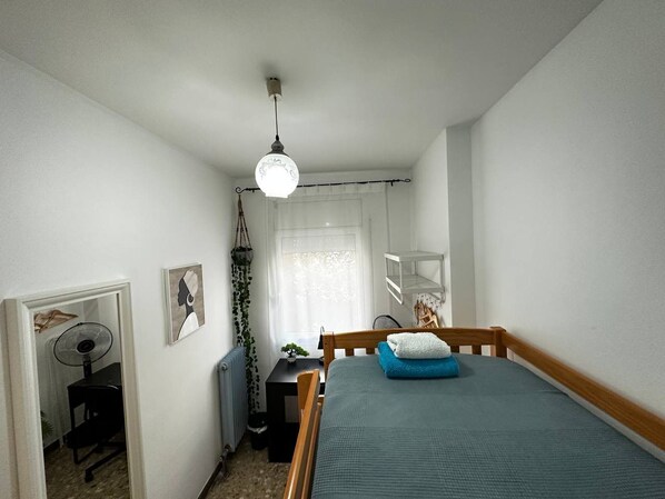 A small, well-lit bedroom with a single bed, a desk, and a hanging plant. - Rooms Sepulveda (Barcelona)
