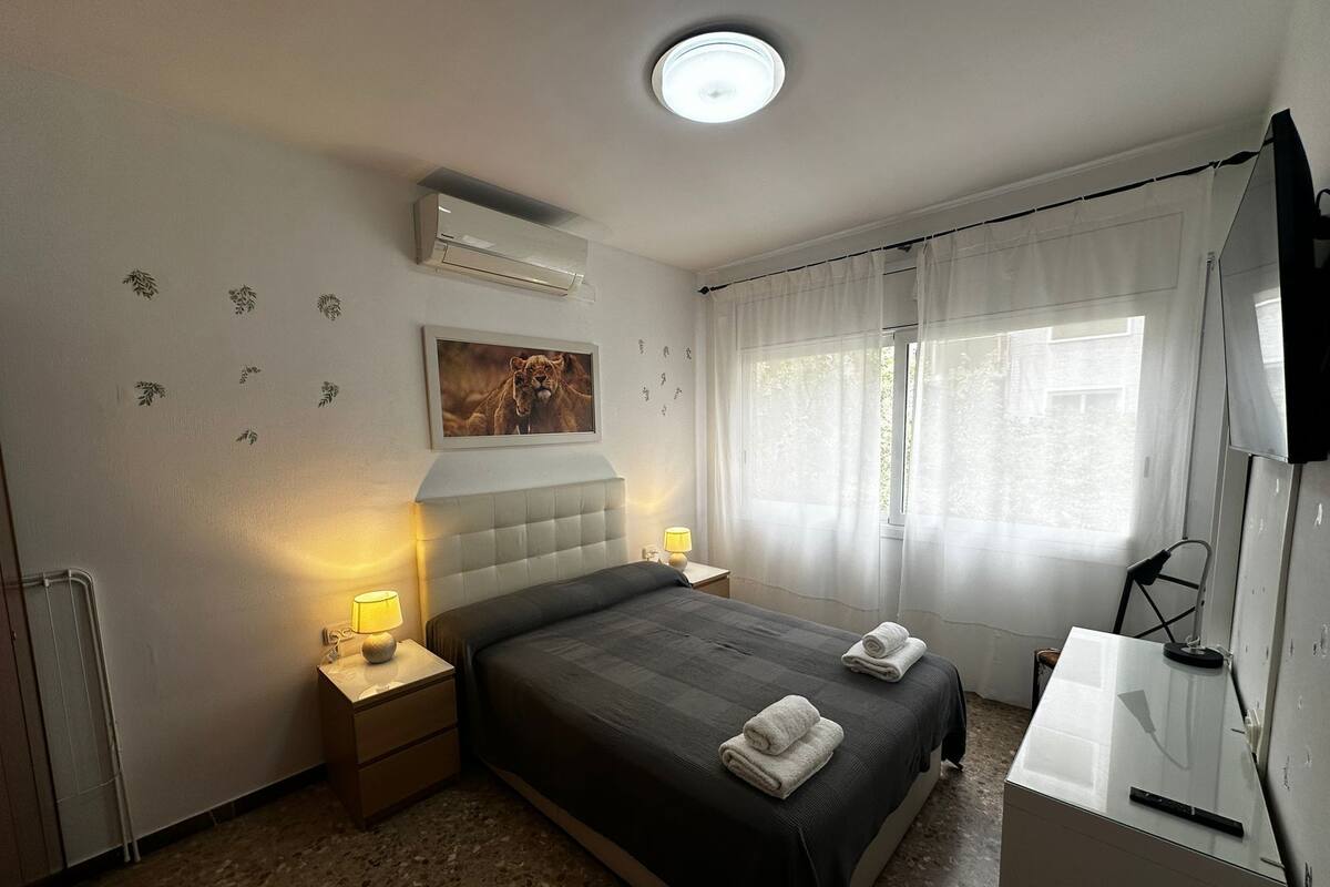 Una camera d'albergo con un letto, abat-jour, una TV a schermo piatto, una finestra con tende e un termosifone.