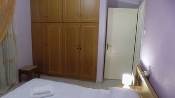 A hotel room with a large wardrobe, a bed with white linens, a bedside table with a lamp, and a door.