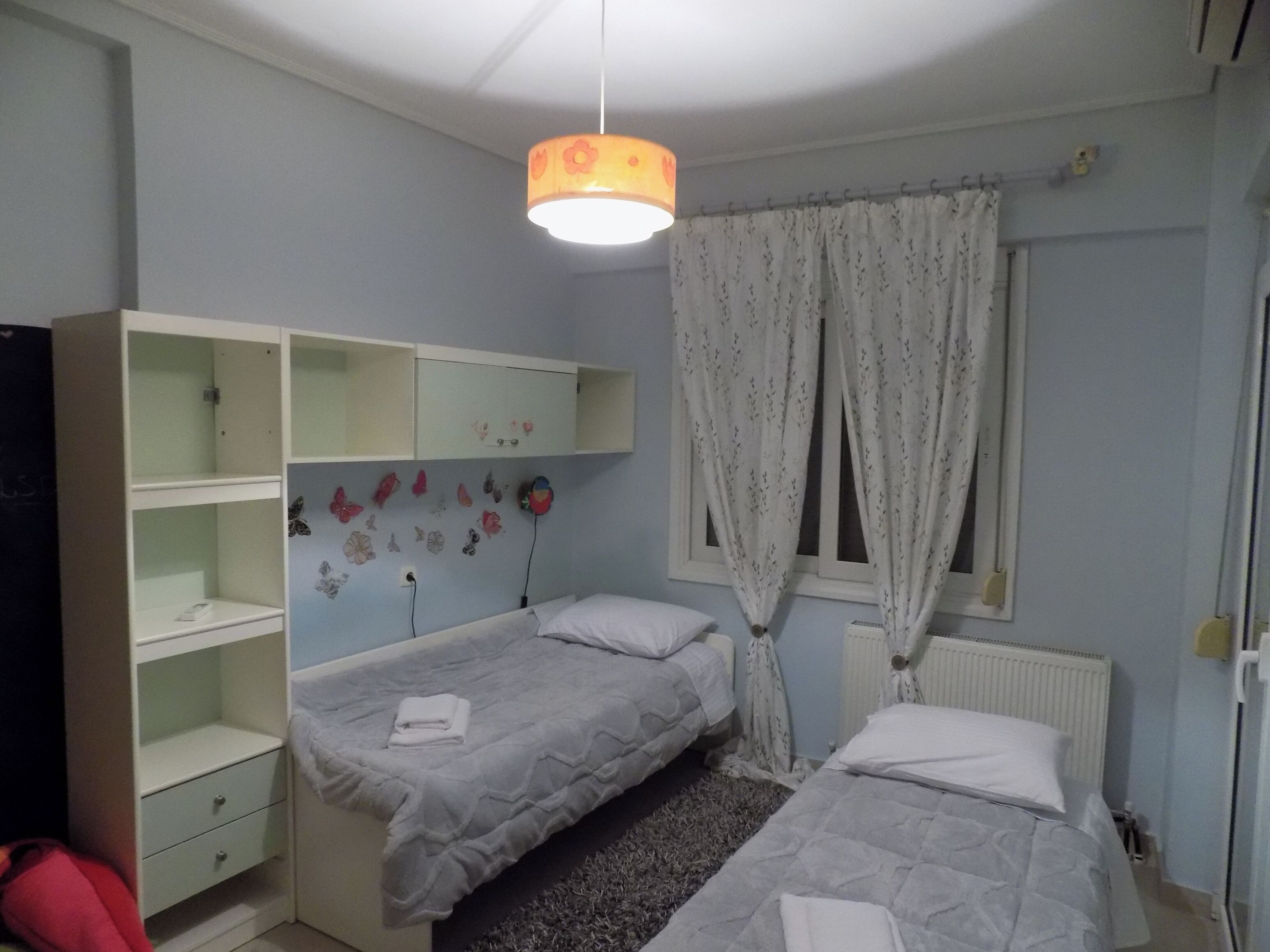 Une chambre avec deux lits, une armoire, un radiateur et une fenêtre avec des rideaux.