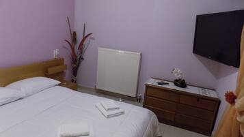 A hotel room with a bed, a bedside table, a dresser, a radiator, and a flat-screen TV mounted on the wall.