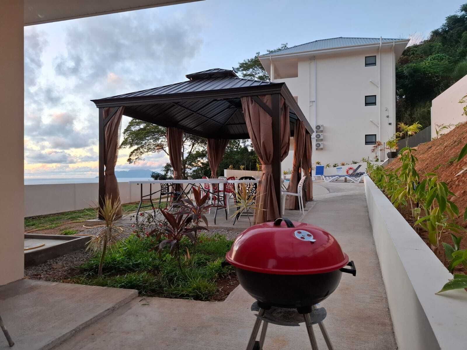 Un espace extérieur aménagé avec un barbecue, un coin salon abrité et une vue sur l’océan.