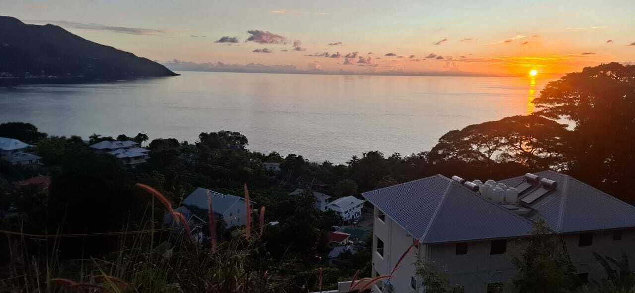 A coastal view with a sunset, houses, and a mountain in the background.