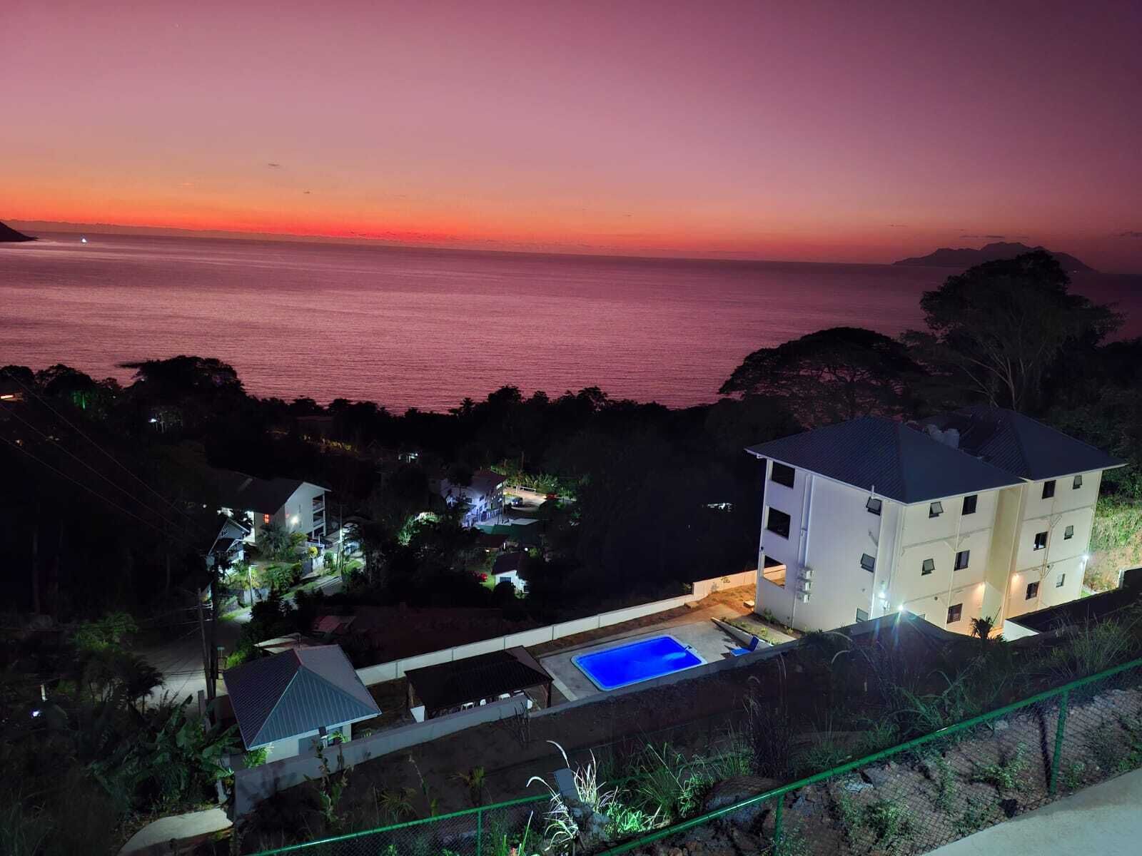Eine Küstenimmobilie mit Schwimmbad, einem mehrstöckigen Gebäude und Blick auf das Meer bei Sonnenuntergang.