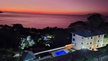Eine Küstenimmobilie mit Schwimmbad, einem mehrstöckigen Gebäude und Blick auf das Meer bei Sonnenuntergang.