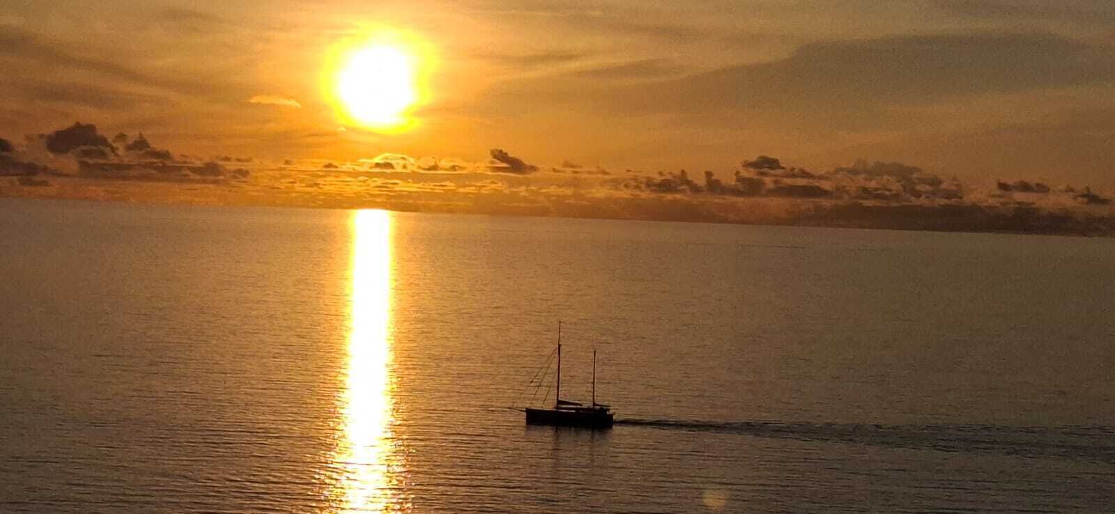 Un bateau sur une eau calme, avec un coucher de soleil en arrière-plan.