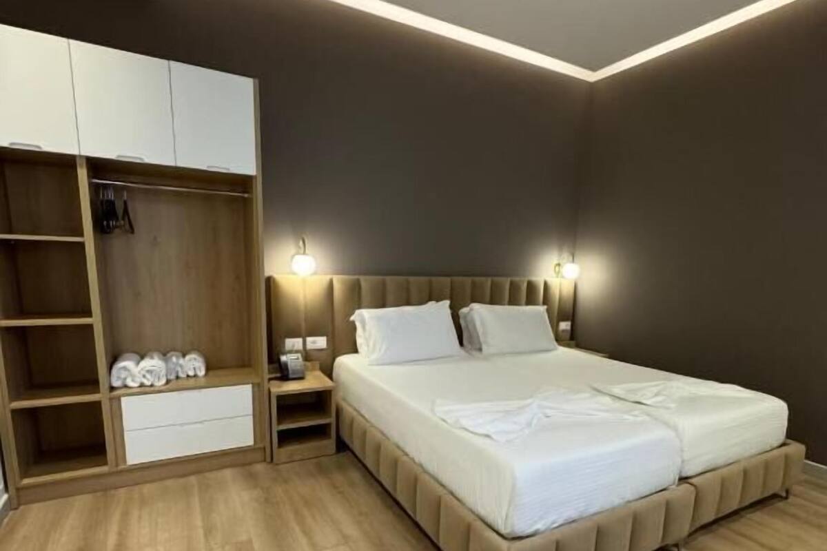 A modern bedroom with a large bed, built-in wardrobe, bedside lamps, and a wooden floor.