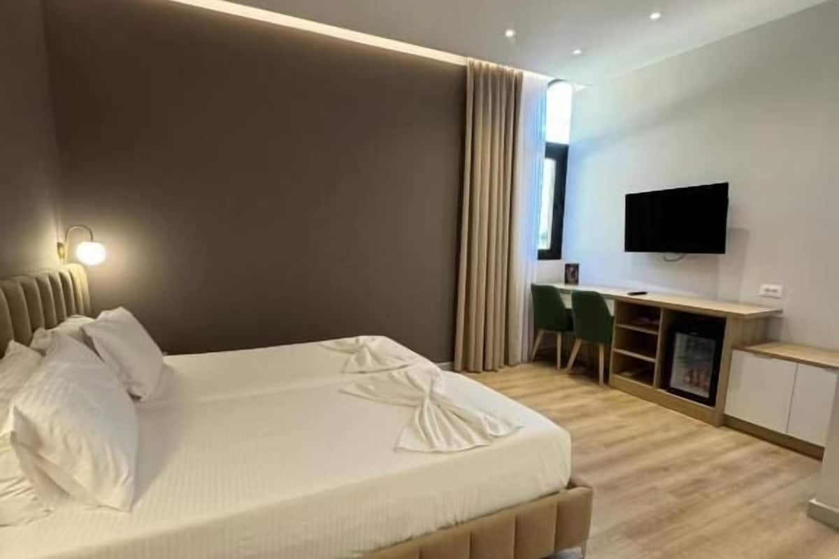 A modern hotel room with a large bed, a desk, a flat-screen TV, and a seating area.