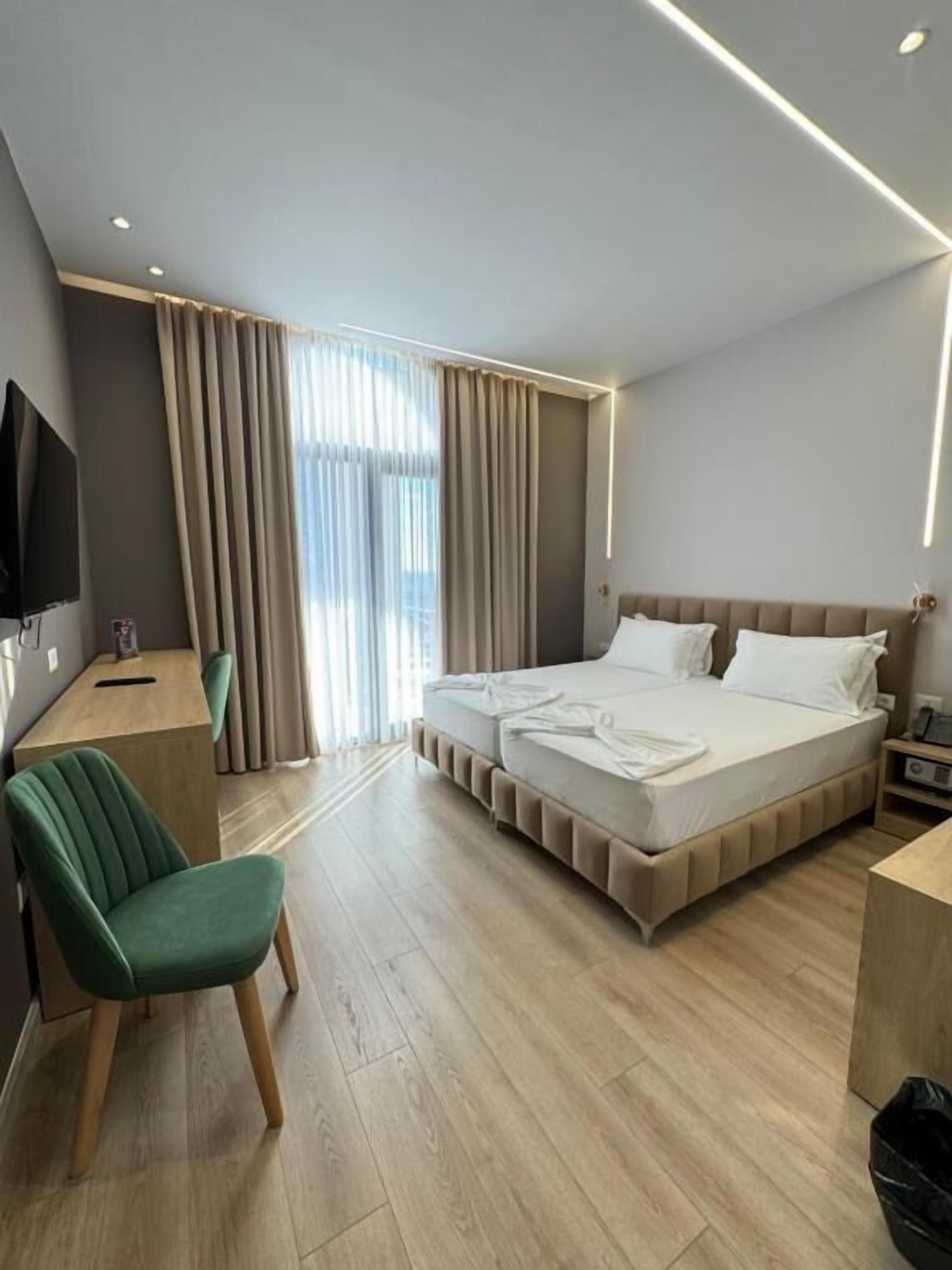 A modern hotel room with a large bed, a desk, a chair, and a television.