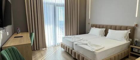 A modern hotel room with a large bed, a desk, a chair, and a television.