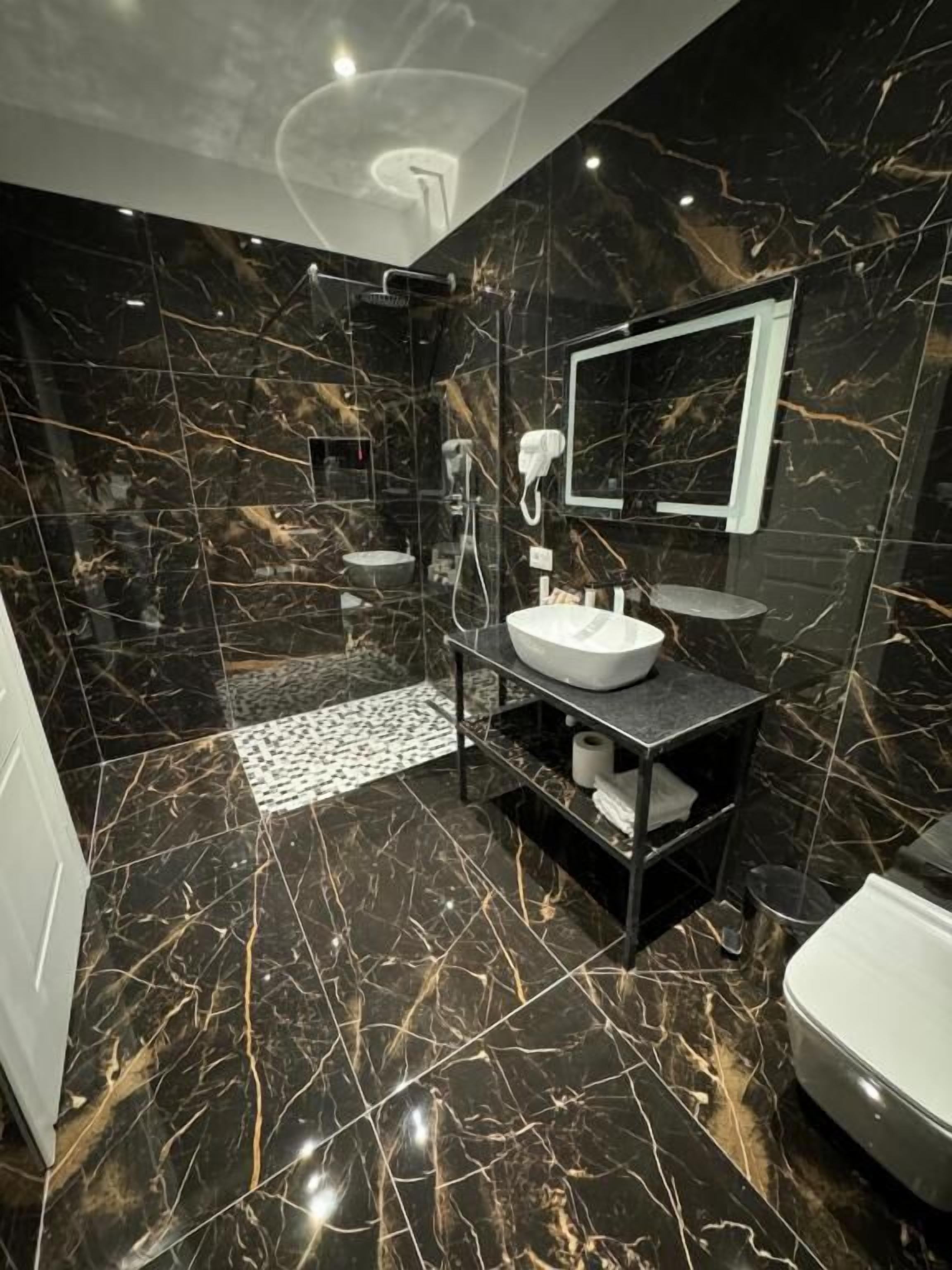 A modern bathroom with a black marble floor, a white sink, a mirror, and a shower area.