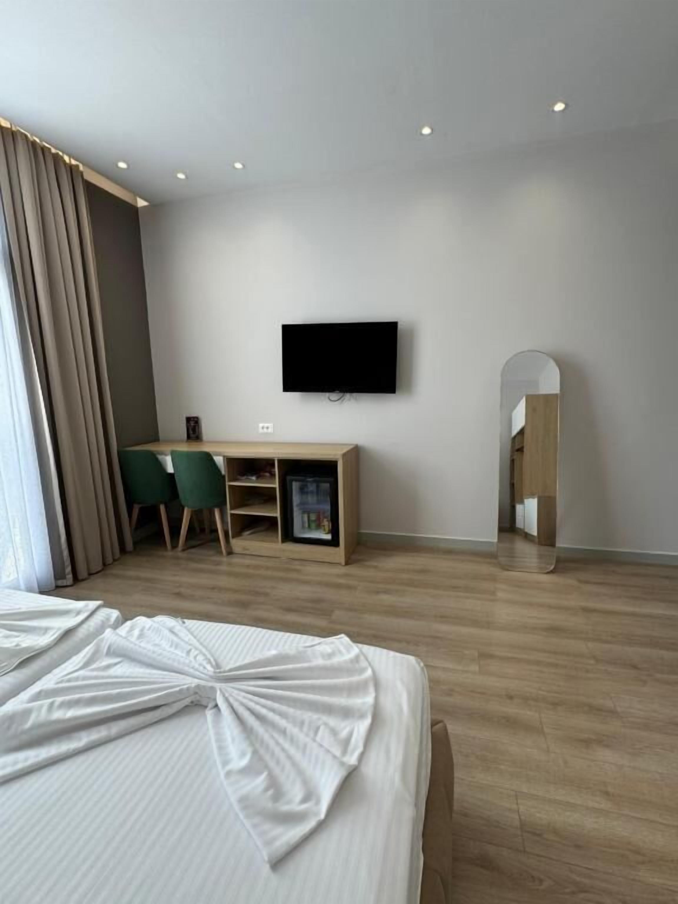 Une chambre d’hôtel moderne dotée d’un grand lit, d’un bureau avec des chaises, d’un téléviseur à écran plat fixé au mur et d’une armoire avec un miroir.
