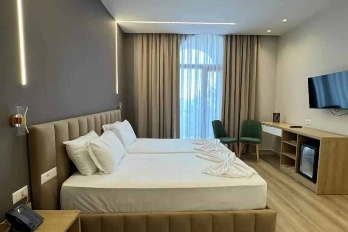 A modern hotel room with a large bed, a desk, a chair, and a television.