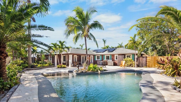 Propiedad residencial con piscina, palmeras y una casa con paneles solares.